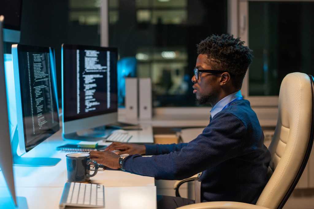 Young it-engineer working with coded data while sitting in armchair in front of computer in office