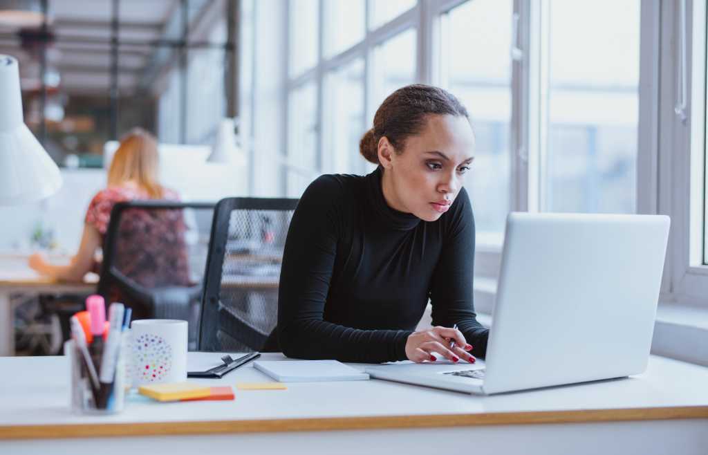 Image of woman using laptop while sitting at her desk. Young african american businesswoman sitting in the office and working on laptop.